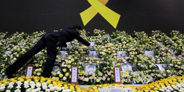 A funeral service employee sets up a group memorial altar for victims of the sunken ferry Sewol in Ansan, south of Seoul, South Korea, Tuesday, April 29, 2014. South Korean President Park Geun-hye apologized Tuesday for the government's inept initial response to a deadly ferry sinking as divers fought strong currents in their search for nearly 100 passengers still missing nearly two weeks after the accident.(AP Photo/Ahn Young-joon)