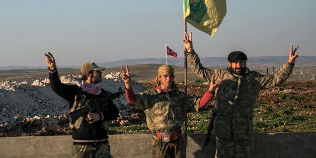 Syrian Kurdish militia members of YPG make V-sign next to poster of Abdullah Ocalan, jailed Kurdish rebel leader, and a Turkish army tank in the background in Esme village in Aleppo province, Syria, Sunday, Feb. 22, 2015. Turkey launched an overnight military operation into neighboring Syria to evacuate troops guarding an Ottoman tomb and to move the crypt to a new location, Turkish Prime Minister Ahmet Davutoglu said Sunday. Davutoglu said they plan to build a new Ottoman tomb in Esme village,