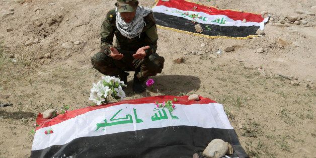 Shiite militiaman prays at a mass grave, believed to contain the bodies of Iraqi soldiers killed by Islamic State group militants when they overran Camp Speicher military base last June, in Tikrit, Iraq,  80 miles (130 kilometers) north of Baghdad, Friday, April 3, 2015. (AP Photo/Khalid Mohammed)