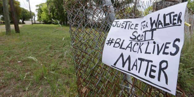 A sign calling for justice is attached to a fence near the site where Walter Scott was killed in North Charleston, S.C., Wednesday, April 8, 2015.  Scott was killed by a North Charleston police officer after a traffic stop on Saturday.  The officer, Michael Thomas Slager, has been charged with murder. (AP Photo/Chuck Burton)
