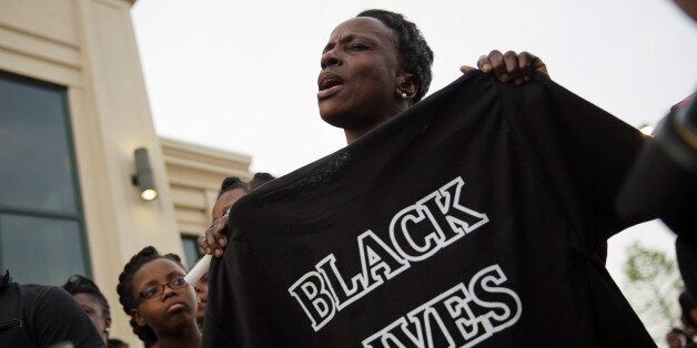 A woman sings while holding a t-shirt during a rally protesting the shooting death of Walter Scott, Friday, April 10, 2015, in North Charleston, S.C. Scott was killed by a North Charleston police officer after a traffic stop on Saturday. The officer, Michael Thomas Slager, has been charged with murder. (AP Photo/David Goldman)
