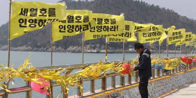An unidentified man reads messages tied with yellow ribbons for the victims of the sunken ferry Sewol at a port in Jindo, South Korea Tuesday, April 14, 2015. Of the 304 people killed when the ferry sank April 16 last year in the waters near Jindo, 295 bodies have been recovered. The letters on flags read: