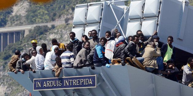 Migrants wait to disembark from the Italian Navy vessel 'Chimera' as a plaque reads in Latin