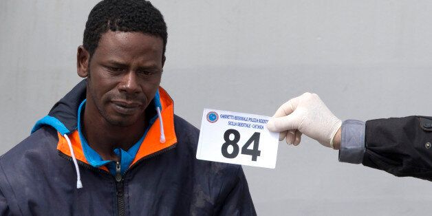 An Italian forensic police officer holds a numbered tag as he identifies a man who disembarked from the Italian Coast Guard ship ' Fiorillo ' at the Catania harbor, Sicily, southern Italy, Friday, April 24, 2015. The European Union's border agency Frontex is to send its ships further into the Mediterranean Sea in response to a deadly exodus of migrants leaving Libya. (AP Photo/Alessandra Tarantino)