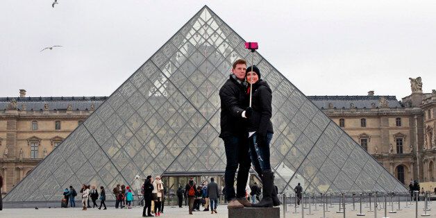 FILE - In this Tuesday, Jan. 6, 2015, Chris Baker and Jennifer Hinson from Nashville, Tennessee, use a selfie stick in front of the Louvre Pyramide in Paris. A French palace and a British museum have joined the growing list of global tourist attractions that have banned âselfie sticksâ _ devices visitors use to improve snapshots, but which critics say are obnoxious and potentially dangerous. Officials at Chateau de Versailles outside Paris and Britainâs National Gallery in London