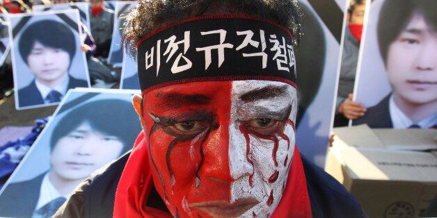 A worker with his face painted, stands in front of portraits of  Choi Jong-beom as he participates in a rally against government's labor policy in front of the Seoul City Hall in Seoul, South Korea, Sunday, Nov. 10, 2013. About 20,000 members of the Korean Confederation of Trade Union demanded better working condition and the end to companies' use of temporary employees. Choi Jong-beom was a Samsung Electronics Service employee, who reportedly killed himself after leaving a message complaining a