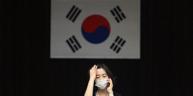 An official wearing a mask as a precaution against the MERS virus works with a South Korean national flag in the background at Dongdaemun District Office in Seoul, South Korea, Thursday, June 18, 2015. The head of the World Health Organization on Thursday praised beleaguered South Korean officials and exhausted health workers, saying their efforts to contain a deadly MERS virus outbreak have put the country on good footing and lowered the public risk. (AP Photo/Ahn Young-joon)