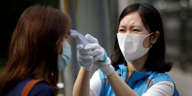 A South Korean health worker from a community health center wearing mask as a precaution against MERS, Middle East Respiratory Syndrome, virus, takes an examinee' temperature at a test site for the civil service examination in Seoul, South Korea, Saturday, June 13, 2015. Experts from the World Health Organization and South Korea have downplayed concerns about the MERS virus spreading further within the country, but they say it's premature to declare the outbreak over. (AP Photo/Lee Jin-man)