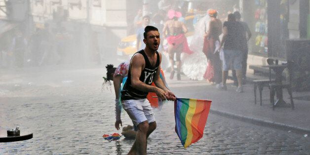 A participant in the Gay Pride event in support of  Lesbian, Gay, Bisexual and Transsexual (LGBT) rights reacts as others flee after Turkish police use a water canon to disperse them in Istanbul, Turkey, Sunday, June 28, 2015. Turkish police have used water cannons and tear gas to clear gay pride demonstrators from Istanbul's central square. Between 100 and 200 protestors were chased away from Taksim Square on Sunday after a police vehicle fired several jets of water to disperse the crowd. It wa