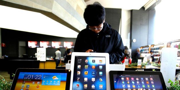A student uses a mobile phone near the Samsung Electronics' new tablet Galaxy Tab 10.1 with Apple's white iPad on display, center, at the showroom in Seoul, South Korea, Monday, Oct. 3, 2011. If Samsung is to live up to the vaulting ambitions of its homeland and its top executives, many feel it must move beyond being a highly efficient imitator to creating products so original and seductive in function and design they become icons of consumer culture. (AP Photo/Lee Jin-man)