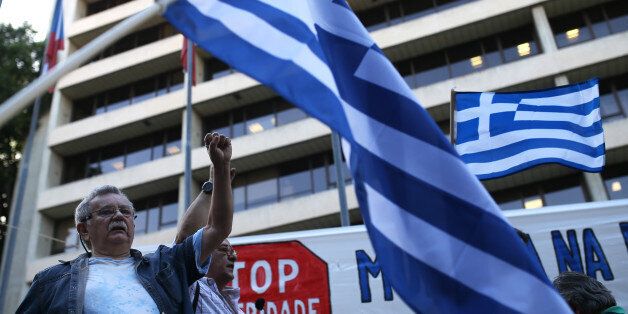 People sing a protest song as others wave Greek flags during a rally in support to the Greek government outside the Jean Monnet European Centre, the European Commission headquarters in Portugal, in Lisbon, Monday, June 29, 2015. Greeks endured the first day of serious controls on their daily economic lives ahead of a July 5 referendum that could determine whether the country has to ditch the euro currency and return to the drachma. (AP Photo/Francisco Seco)