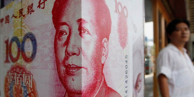 A man stands next to a copy of the Chinese RMB at a money exchange store in Hong Kong Friday, July 20, 2012. (AP Photo/Kin Cheung)