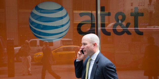 A man using a mobile phone walks past an AT&T store, Tuesday, June 23, 2015 in New York. (AP Photo/Mark Lennihan)