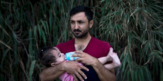 A Syrian refugee feeds milk to his daughter after they arrived on a dinghy, from Turkey to Lesbos island, Greece, Wednesday, Sept. 9, 2015. The head of the European Union's executive says 22 of the member states should be forced to accept another 120,000 people in need of international protection who have come toward the continent at high risk through Greece, Italy and Hungary. (AP Photo/Petros Giannakouris)