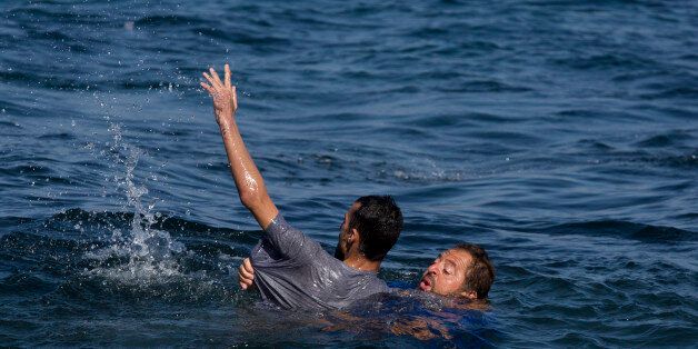 Local resident Dimitris Karapanagiotis, right,  rescues an Afghan migrant whose boat stalled at sea while crossing with others from Turkey to the island of Lesbos, Greece, on Saturday, Sept. 19, 2015. A girl about five years old died and at least 13 undocumented refugees and migrants were missing on Saturday after a boat transferring dozens of people from Turkey to Greece overturned off Lesbos island, Greek Coast Guard said. (AP Photo/Petros Giannakouris)