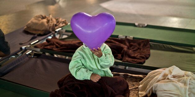 An Afghan refugee child covers his face with a balloon while he and other migrants spent the night in a shelter near Graz, Austria, Tuesday, Sept. 22, 2015. Hungary's prime minister Viktor Orban said that millions of migrants are
