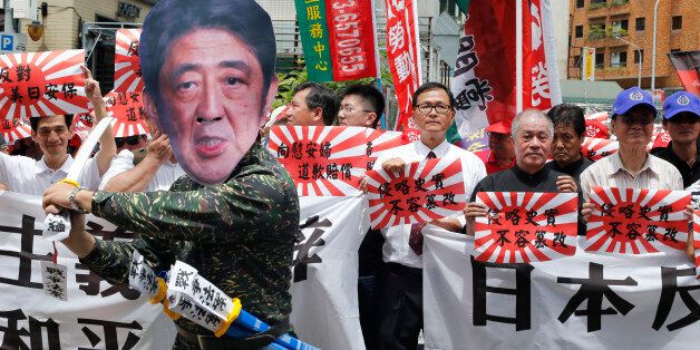 An activist dressed as Japanese Prime Minister Shinzo Abe poses with Japanese military flags reading