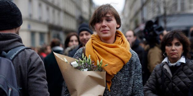 A woman carrying flowers cries in front of the Carillon cafe and the Petit Cambodge restaurant in Paris Saturday Nov. 14, 2015, a day after over 120 people were killed in a series of attacks in Paris. French President Francois Hollande said at least 127 people died Friday night when at least eight attackers launched gun attacks at Paris cafes, detonated suicide bombs near France's national stadium and killed hostages inside a concert hall during a rock show. (AP Photo/Jerome Delay)