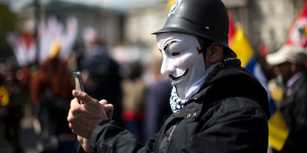 A protester wearing a toy British police helmet and an Anonymous mask takes a picture during a rally at the end of a May Day demonstration march in Trafalgar Square in London, Friday, May 1, 2015. Tens of thousands of workers marked May Day in European cities with a mix of anger and gloom over austerity measures imposed by leaders trying to contain the eurozone's intractable debt crisis. (AP Photo/Matt Dunham)