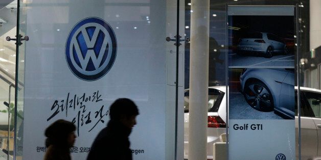 People walk by a logo of Volkswagen at a dealership in Seoul, South Korea, Thursday, Nov. 26, 2015.  South Korea said Thursday it fined Volkswagen $12.3 million and ordered recalls of 125,522 diesel vehicles after the government found their emissions tests were rigged. (AP Photo/Ahn Young-joon)