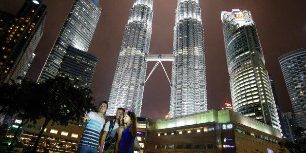 Tourists take souvenir photographs against Malaysia's iconic building, Petronas Twin Towers in Kuala Lumpur, Malaysia, Thursday, Jan. 14, 2016. Malaysia's national police chief Khalid Abu Bakar says police have raised security alert to the highest level following the deadly attack in Jakarta. (AP Photo/Joshua Paul)