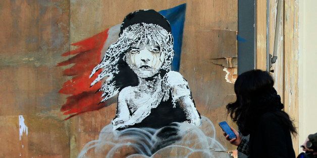 Commuters take photos on their phones of a new artwork by British artist Banksy opposite the French Embassy, in London, Monday, Jan. 25, 2016. The artwork depicts the young girl from the musical Les Miserables with tears streaming from her eyes as a can of CS gas lies beneath her. The work is criticising the use of teargas in the refugee camp in Calais. (AP Photo/Alastair Grant)