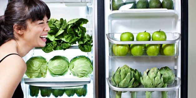 Mixed race woman looking at green vegetables in refrigerator