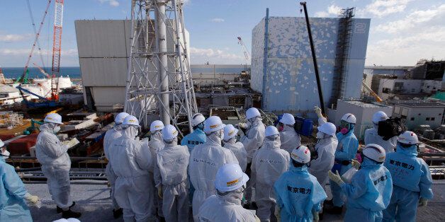 Members of the media tour group, wearing protective suits and masks, receive a briefing from Tokyo Electric Power Co. (TEPCO) employees (in blue) in front of the No. 1, left,and No. 2 reactor buildings at the tsunami-crippled Fukushima Dai-ichi nuclear power plant in Okuma, Fukushima Prefecture, northeastern Japan, Wednesday, Feb. 10, 2016. In one month, Japan is marking the fifth anniversary of a devastating earthquake and tsunami that hit on March 11, 2011 and left nearly 19,000 people dead or