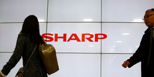 People walk past the log of Sharp Corp. in Tokyo, Thursday, Feb. 25, 2016. Troubled Japanese electronics maker Sharp has agreed to a takeover offer from Taiwanese company Hon Hai, also known as Foxconn, Japanese media reported Thursday. (AP Photo/Shizuo Kambayashi)