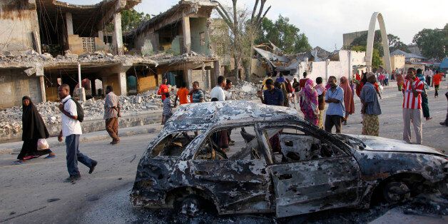 Somalis walk near destroyed buildings and the wreckage of a car, Saturday, Feb. 27, 2016 after a suicide car bomb Friday night in Mogadishu, Somalia. A suicide bomber rammed his car into the SYL hotel's entrance in Mogadishu and blew it up, allowing gunmen to fight their way past hotel guards at the first security barrier, said Capt. Mohamed Hussein. (AP Photo/Farah Abdi Warsameh)