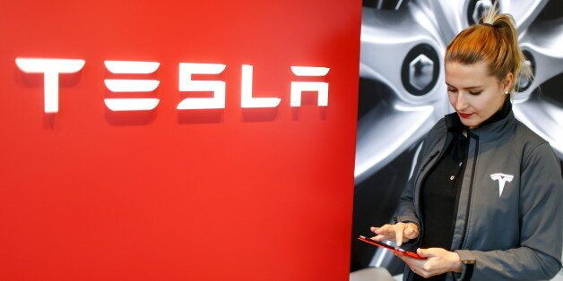 A Tesla employee stands beside a company logo in the dealership in Berlin, Germany, November 18, 2015. REUTERS/Hannibal Hanschke