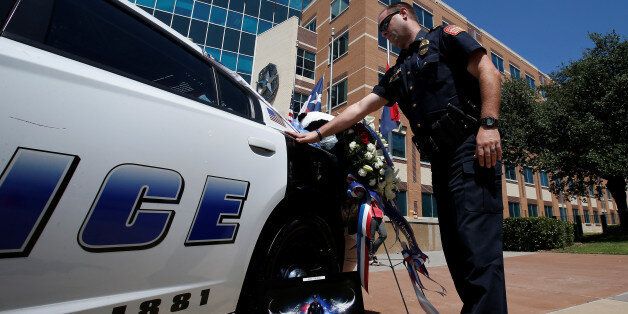 An officer touches a police car during a personal moment of silence at a makeshift memorial at Police Headquarters following the multiple police shooting in Dallas, Texas, U.S.,July 8, 2016.  REUTERS/Carlo Allegri
