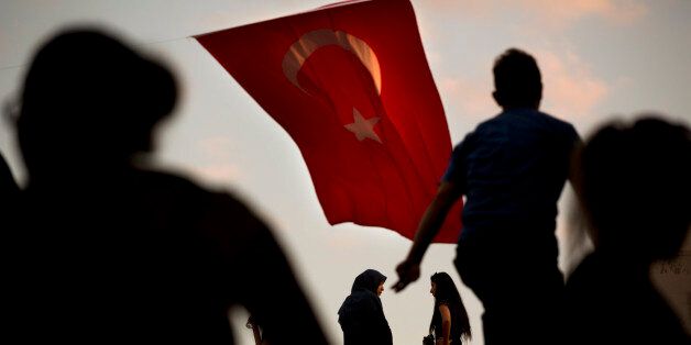People walk by a Turkish flag in central Istanbul, Monday, July 18, 2016. Turkey's Interior Ministry has fired nearly 9,000 police officers, bureaucrats and others and detained thousands of suspected plotters following a foiled coup against the government, Turkey's state-run news agency reported Monday. (AP Photo/Emilio Morenatti)