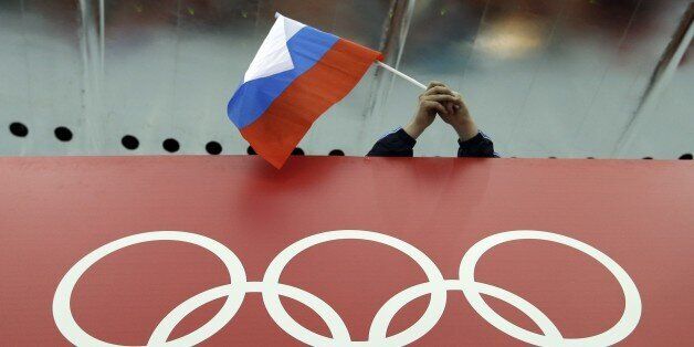 FILE - In this Feb. 18, 2014 file photo, a Russian skating fan holds the country's national flag over the Olympic rings before the start of the men's 10,000-meter speedskating race at Adler Arena Skating Center during the 2014 Winter Olympics in Sochi, Russia. The IOC's ruling 15-member executive board will meet Sunday, July 24, 2016 via teleconference to weigh the unprecedented step of excluding Russia as a whole from the 2016 Rio Olympic Games because of systematic, state-sponsored cheating. (
