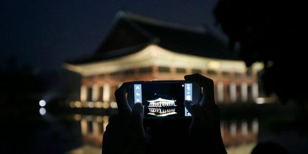 A visitor takes a photograph of Gyeonghoeru pavilion, a part of Gyeongbok palace, during the evening in central Seoul May 23, 2013. Gyeongbok Palace offered late-night admissions to the public from Wednesday until Sunday, The Cultural Heritage Administration said.   REUTERS/Kim Hong-Ji (SOUTH KOREA - Tags: TRAVEL)