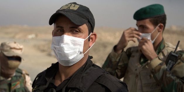 Iraqi troops wear masks as they guard a checkpoint near the village of Awsaja, Iraq, as smoke from fires lit by Islamic State militants at oil wells and a sulfur plant fills the air. U.S. military officials say that a fire at a sulfur plant in northern Iraq set by Islamic State militants on Thursday is creating a potential breathing hazard for American forces and other troops at a logistical base south of Mosul. (AP Photo/Adam Schreck)