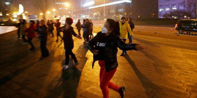 A woman wearing masks and other residents dance during their daily exercise amid the heavy smog in Beijing, China December 7, 2015. China's capital on Monday issued its first ever