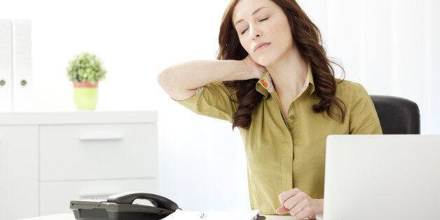 Young Businesswoman Having Neckache in the office, doing massage of the neck and sitting at the desk.