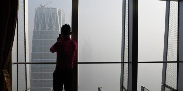 A man takes photos of buildings on a polluted day in Beijing on January 1, 2017. China's capital city started the year under a heavy blanket of grey smog, with a concentration of toxic particles 20 times higher than the maximal level recommended by the World Health Organization, as a new pollution cloud was - again - striking the country. / AFP / GREG BAKER        (Photo credit should read GREG BAKER/AFP/Getty Images)