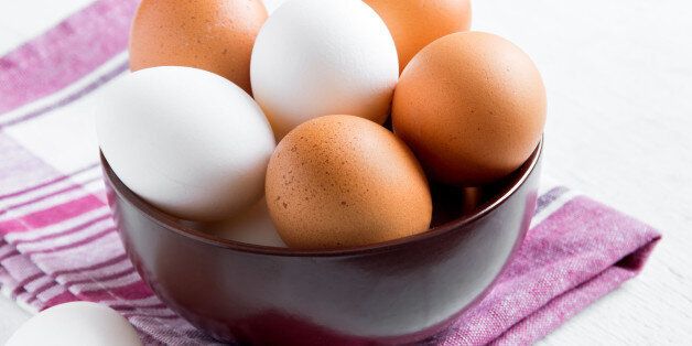 Raw organic brown and white eggs in bowl over linen napkin and wooden background