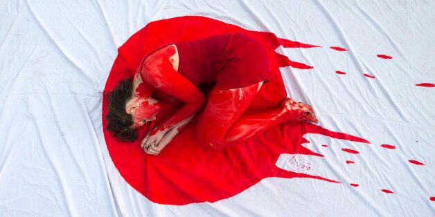 An Israeli member of the 'Taiji Dolphin Action Group', with a red body painting to evok blood, is curled up on a sheet depicting the Japanese flag, during a protest against the killing of dolphins, notably in the Japanese city of Taiji on January 30, 2014 outside the building housing the Japanese Embassy, in the Mediterranean coastal city of Tel Aviv. Similar rallies outside Japanese consulates and embassies were expected to take place worldwide. AFP PHOTO / JACK GUEZ        (Photo credit should