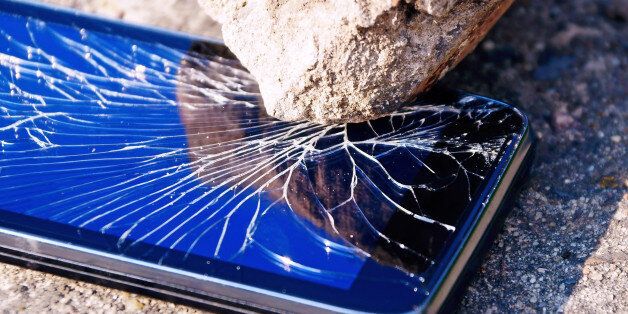 Cracked mobile smartphone savagely smashed by a stone.