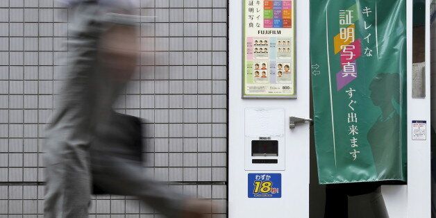 A pedestrian walks past an ID photo machine box as a man sits inside at a business district in Tokyo, September 15, 2015. The Bank of Japan said on Tuesday that slowing emerging market demand was putting further strains on the economy but held off on expanding stimulus, preserving its limited policy options in case an expected U.S. rate hike sparks more global volatility. REUTERS/Yuya Shino