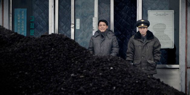 This picture taken on December 14, 2012 from China's northeastern city of Dandong, looking across the border, shows a North Korean military officer (R) and a North Korea man (L) standing behind a pile of coal along the banks of the Yalu River in the northeast of the North Korean border town of Siniuju.  China is North Korea's biggest trading partner by far, and most of the business passes through Dandong in northeastern China, where lorries piled high with tyres and sacks are processed at the cu