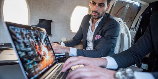 Focus on well dressed businessmen in the back while looking at the screen of his colleague's laptop.