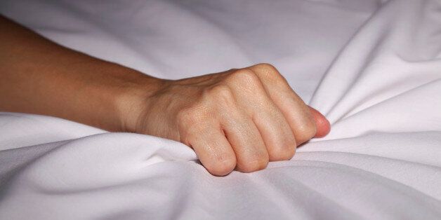 Woman's hand grabbing bed sheets during an orgasm