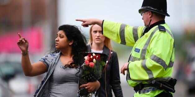 A police officer (R) directs a woman carrying a bunch of flowers near the Manchester Arena in Manchester, northwest England on May 23, 2017 following a deadly terror attack at the concert at the venue the night before. Twenty two people have been killed and dozens injured in Britain's deadliest terror attack in over a decade after a suspected suicide bomber targeted fans leaving a concert of US singer Ariana Grande in Manchester. / AFP PHOTO / Oli SCARFF        (Photo credit should read OLI SCAR