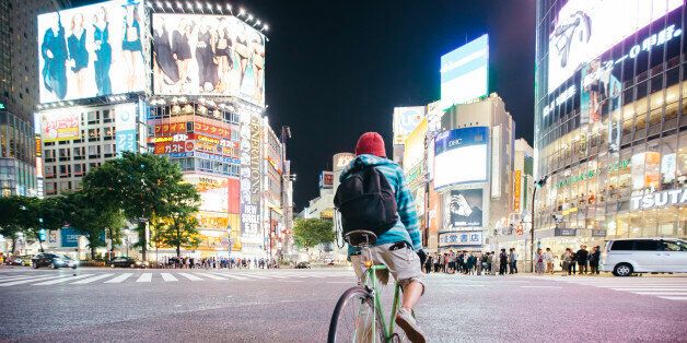 Young guy with backpack riding a bike on Shibuya crossing in Tokyo, Japan