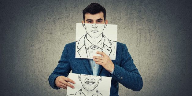 Businessman holding two white papers with different emotions drawn, one hiding half face with angry expressionon and another with a happy, smiling face. Switch mask to hide identity concept.