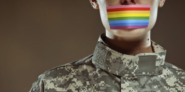 A lesbian female U.S. Army soldier saluting with a gay pride rainbow covering her mouth.